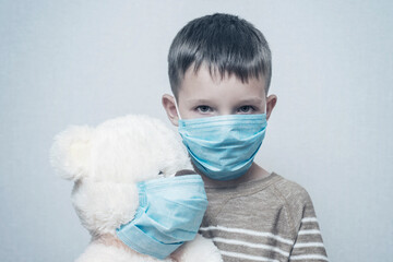 A sad child holds his teddy bear, both wearing protective medical masks. Coronavirus quarantine. Prevention epidemic