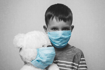 A sad child holds his teddy bear, both wearing protective medical masks. Coronavirus quarantine. Prevention epidemic