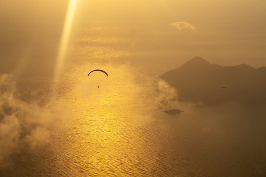 Silhouette of paraglider soaring over sea at sunset light