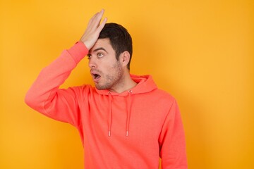 Handsome man with sweatshirt over isolated yellow background surprised with hand on head for...