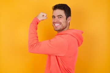 Handsome man with sweatshirt over isolated yellow background praying for luck has hands crossed near face, amazed and opening mouth looking front.