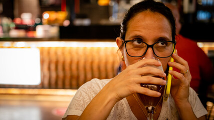 Young beautiful woman with her phone sitting in a restaurant with a glass of beer
