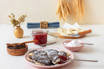 Pastry parcels filled with plum marmalade, dusted with poppy seed and icing sugar. Tasty poppy seed dessert or main course. White wooden table background. Low angle view.