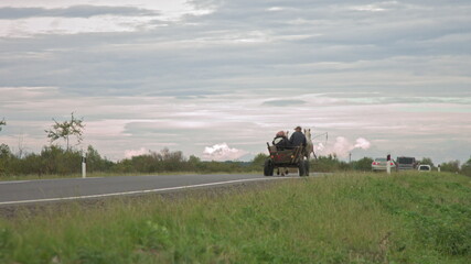 on the new road after repair peasants go on fires and horses, old transport, poor people on transport are overtaken by modern cars, people out of modern civilization