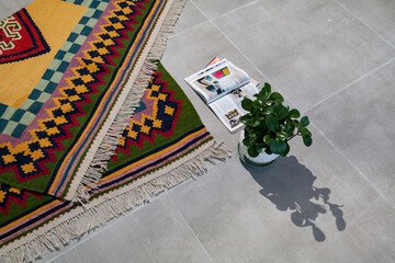 A hand woven and knotted Persian colorful kilim on the floor with magazines and flower pot 