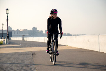 Woman athlete cyclist rides a bicycle along the embankment at sunrise