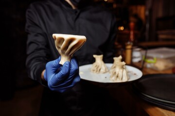 a waiter in a glove holds a khinkali in his hand