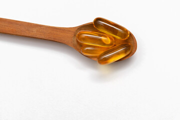 fish oil capsules in a wooden spoon on a white background