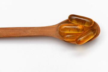 fish oil capsules in a wooden spoon on a white background