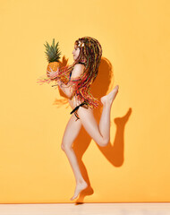 Girl jumps with a pineapple in her hands in profile on a yellow background.