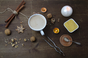 top view on a wooden old table, where a white cup with cappuccino coffee, a cup with honey, nuts, a nut cracker and sweets are lying, candles are burning