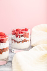 Yogurt with raspberry, goji berries and chia seeds in glass on gray and pink background. Side view, copy space.