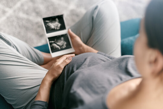 Pregnant woman sitting on the sofa and watching ultrasound images of her baby