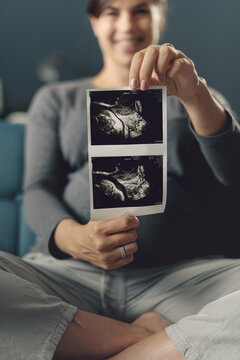 Happy pregnant woman showing ultrasound images of her baby