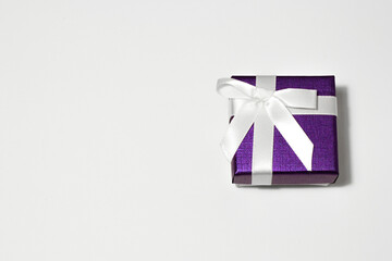 Small purple gift box with a white ribbon on a white background with copy space.