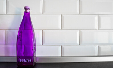 Purple glass bottle for water and other drinks with the text inspiration on the white tile background