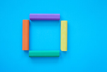 Square made from colorful chalk sticks isolated on blue background; close up of chalks in various colors; children's stationery; creativity material; picture frame; flat lay, top view, copy space