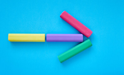 An arrow pointing to the right made of colorful chalk sticks isolated on blue background; close up of chalks in various colors; children's stationery; creativity material; flat lay, top view