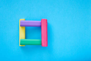 Square made from colorful chalk sticks isolated on blue background; close up of chalks in various colors; children's stationery; creativity material; picture frame; flat lay, top view, copy space