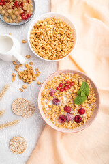 Wheat flakes porridge with milk, raspberry and currant in ceramic bowl on gray concrete background. Top view, close up.