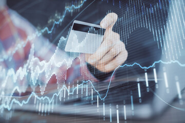 Double exposure of man hands holding a credit card and Forex graph drawing. Stock trading and digital fintech in Internet E-commerce concept.