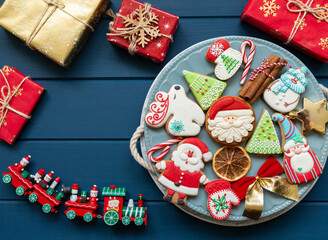 Homemade christmas gingerbread cookies and presents  on plate on classic blue wooden background. Snowflake, star, tree, snowman, deer shapes. Holiday, celebration and cooking concept. Close up.	