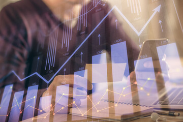 Double exposure of man's hands holding and using a phone and financial graph drawing. Analysis...
