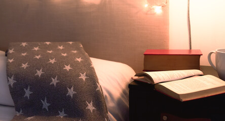 Tiempo de leer y relajarse antes de irse a dormir. Primer plano de mesa de noche con un par de libros y un taza de café junto a una cama en una confortable y calidamente iluminada habitación.
