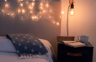 Tiempo de leer y relajarse antes de irse a dormir. Primer plano de mesa de noche con un par de libros y un taza de café junto a una cama en una confortable y calidamente iluminada habitación.