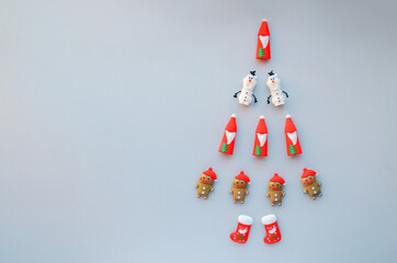 Creative walking Christmas tree made of New Year symbols decorations on grey background. Santa, snowman, gingerbread man, snow boot on Holiday card. Minimal concept, flat lay, copy space, top view.
