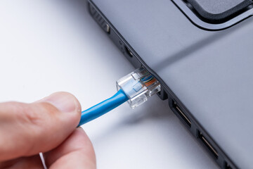 person plugging internet ethernet cable to laptop pc. online and network access conceptual....