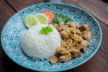 Fried chicken with garlic and pepper over rice is on blue plate and brown wood as a background.