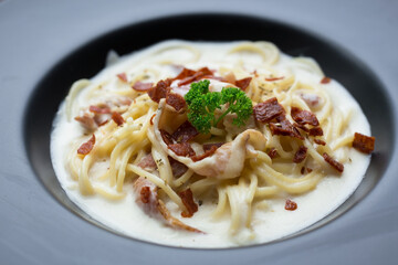 Spaghetti carbonara with a white sauce and on top with crispy bacon and parsley.