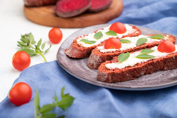 Red beet bread sandwiches with cream cheese and tomatoes on white concrete background. Side view, selective focus.