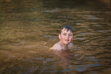 Boy swimming in river at dusk looking up at camera. Springtime fun in New South Wales, Australia
