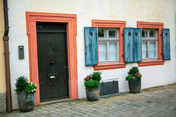 Fototapeta na wymiar Black door and windows with shutters . Rustic house facade with flowerbeds