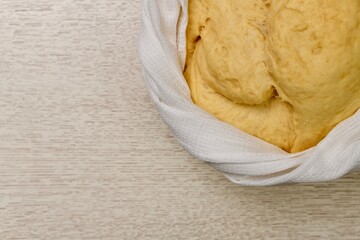  The puffed yeast dough has risen in a bowl. Tied around with a braided white waffle towel.