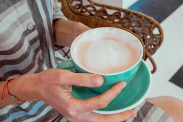 Close up view female hands holding green coffee mug of  cappuccino. Young attractive woman relaxes, drinks warm beverage. 