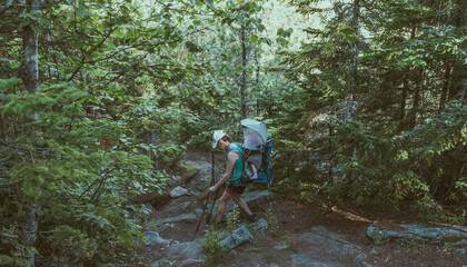 Obraz premium Woman hiking with a baby on a backpack moving among the rocks