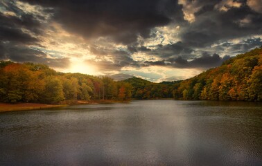 This epic nature image shows a glowing late evening sun over a calm and secluded tree lined lake with leaves turning into beautiful autumn colors.