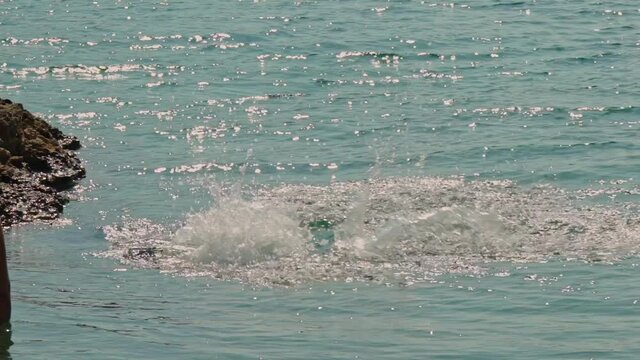 Caucasian boy jumps from rocks to sea for the first time, while his mother watching, slow motion