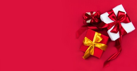 Christmas gift boxes with red and gold ribbons on a red banner background. Christmas and new year banner. Flat lay, top view, copy space, banner