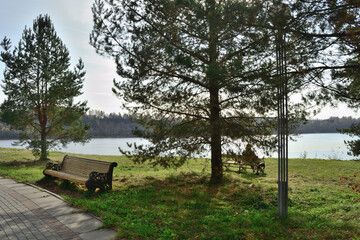 Benches for pleasant relaxation in the park by the river against the background of the autumn forest and sky.