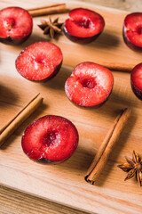 Sliced red plums with cinnamon sticks and anise stars on the wooden table. Selective focus. Shallow depth of field.