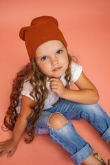 Stylish little girl 6 years old with curly hair in a fashionable hat and ripped jeans