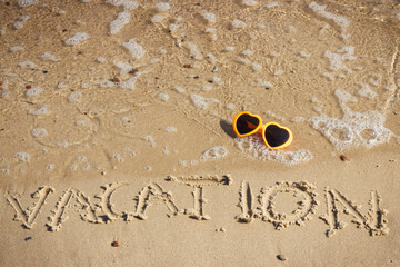 Inscription vacation, sunglasses and sea wave on sand at beach. Summer time