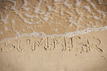 Inscription summer and incoming sea wave on sand at beach. Travel and vacation time