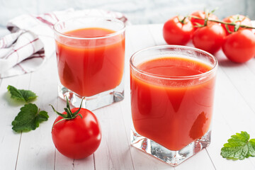 Tomato juice in glass glasses and fresh ripe tomatoes on a branch. White wooden background with copy space.