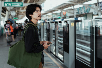 Side view asian man using smartphone at train station.