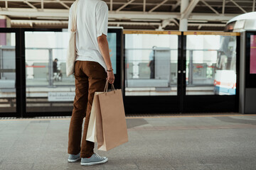 Man holding shopping plastic bag waiting for a train.